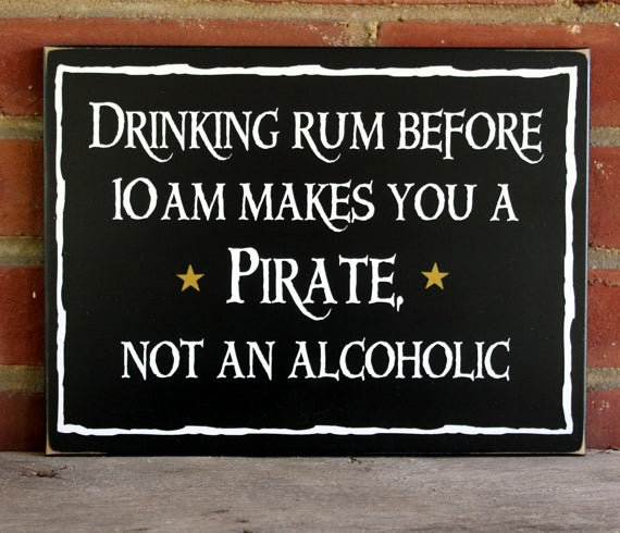 A black worn finish sign saying Drinking rum before 10am makes you a pirate not an alcoholic.  Sign has a white border aound it and a gold star on either side of the word pirate. Available in 2 sizes.   