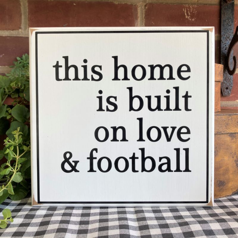 This Home is Built on Love and Football in black lettering on a white worn finish wood sign.  Sign measures 8x8 inches or 12x12 inches. Made in Maryland. 
