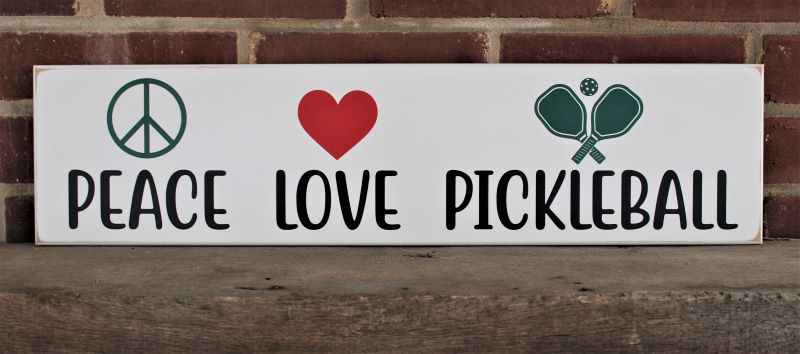 Peace Love Pickleball Fun sign for the Pickleball players in your house. Great gift idea. Worn white finish with words in black and green peace sign, paddles and ball and a bright red heart. Sign measures 6x24 inches.