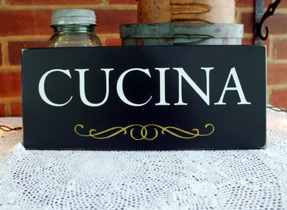 Black wood sign with capital white letters spelling the word CUCINA.  Gold flourish below the lettering. Available  in 2 sizes and several colors. 