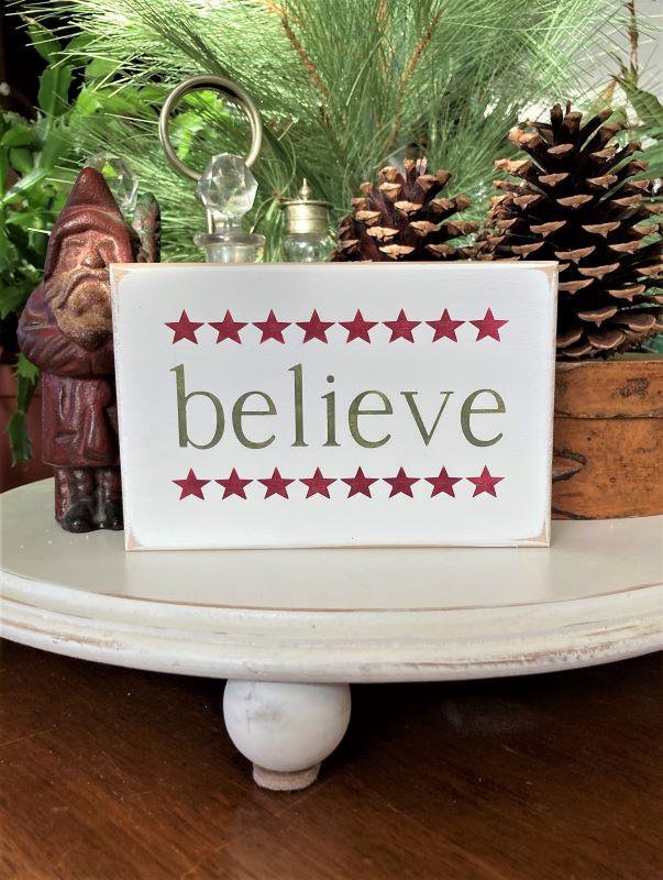 Mini Christmas wood sign. Measures 4x6 inches. Hand painted green lettering saying believe. A line of burgundy stars above and below the word believe.