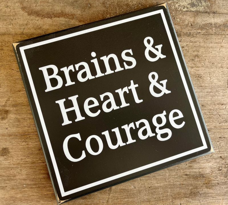 Wizard of Oz Wood Sign. Blaclk worn finish background with white wording that says, Brains & Heart & Courage. Available in two sizes.