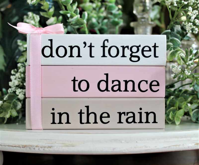 Set of 3 stacking blocks in white, pink and tan with black lettering saying don't forget to dance in the rain.  Blocks are glued together and tied with a bow. A wonderful reminder to take some time for yourself. 