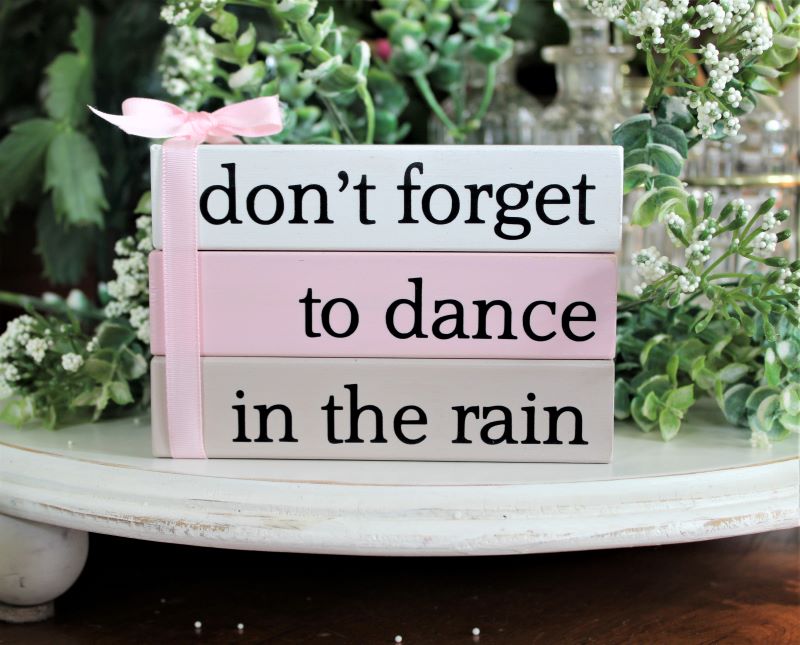 Set of 3 stacking blocks in white, pink and tan with black lettering saying don't forget to dance in the rain. Blocks are glued together and tied with a bow. A wonderful reminder to take some time for yourself.