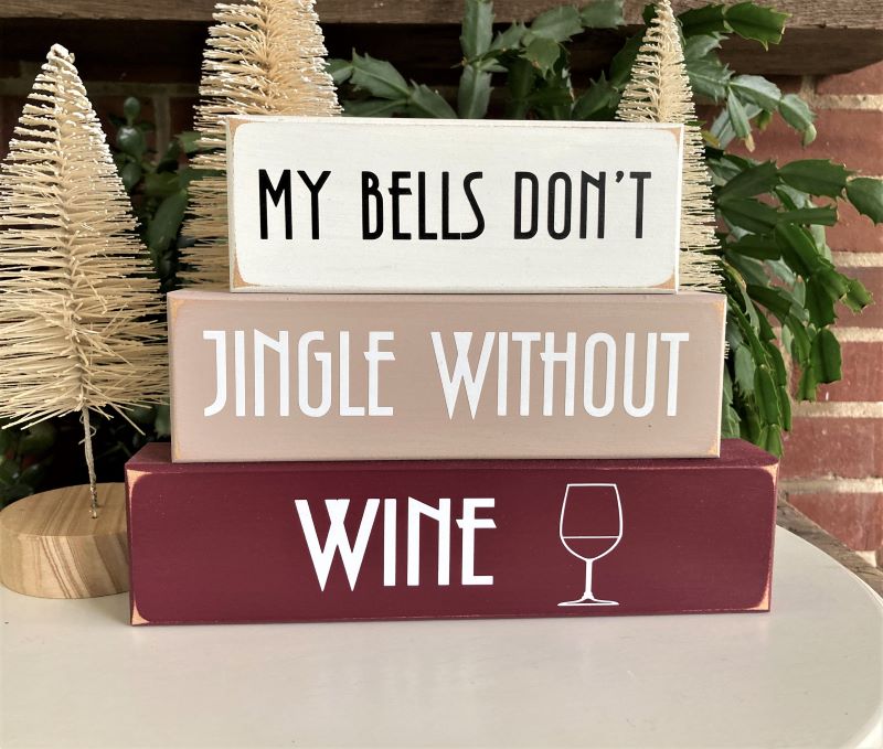 Set of 3 blocks. Top block white with black letters saying MY Bells Don't. Middle block tan with white letters saying Jingle Without. Bottom block burgundy with white lettering saying Wine and a graphic of a wine glass. 6 3/4 h x 9 w x 1 1/2 inches.