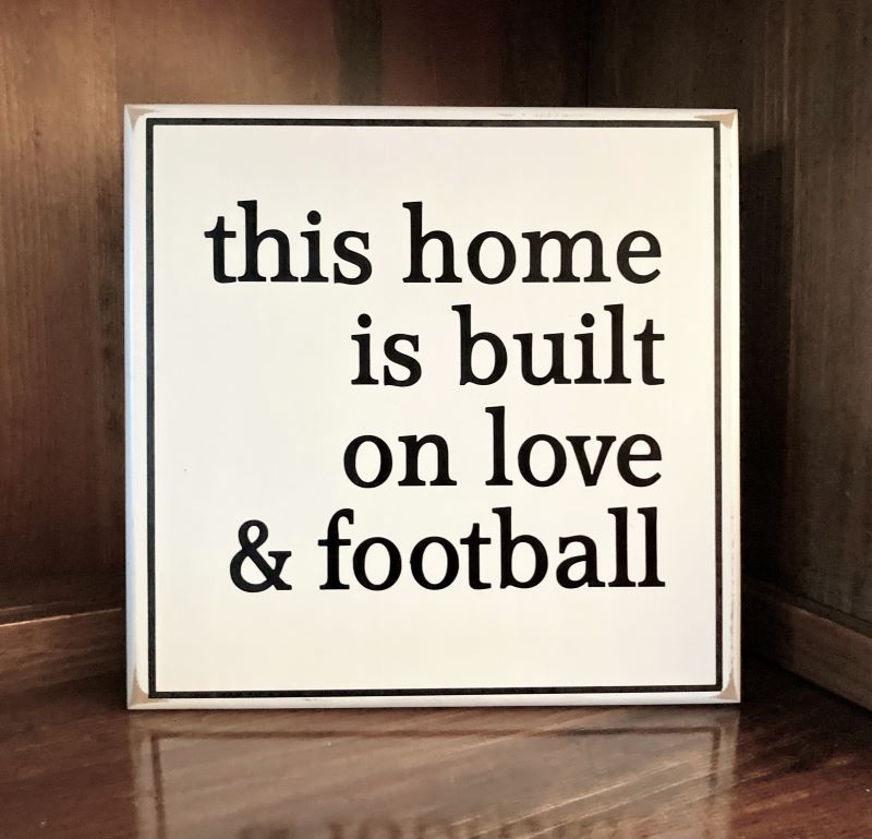 This Home is Built on Love and Football in black lettering on a white worn finish wood sign. Sign measures 8x8 inches or 12x12 inches. Made in Maryland.