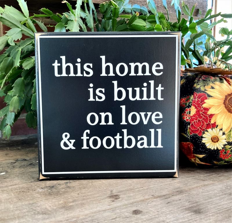 This Home is Built on Love and Football in white lettering on a black finish wood sign. Sign measures 8x8 inches or 12x12 inches. Made in Maryland.