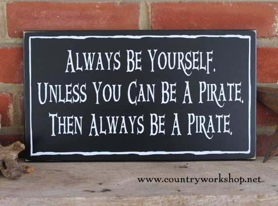 Black worn finish wood sign with white lettering saying Always be yourself unless you can be a pirate, then always be a pirate. Available in 2 sizes. 
