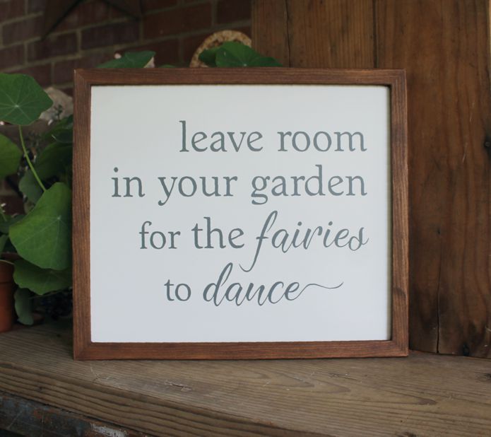 The saying Leave Room in Your Garden for the Fairies to Dance  in gray lettering on a white sign.  Sign has a stained wood frame . Measure 13x15 inches.