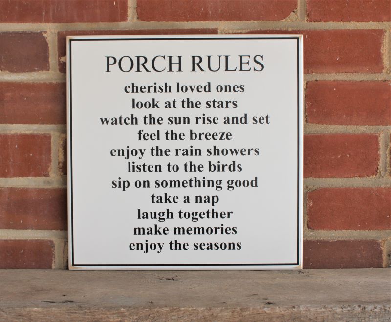 White worn finish square wood sign with black lettering saying.Porch Rules Cherish loved ones Look at the stars Watch the sun rise & set Feel the breeze Enjoy the rain showers Listen to the birds Sip on something good Take a nap Laugh together Make memories Enjoy the seasons