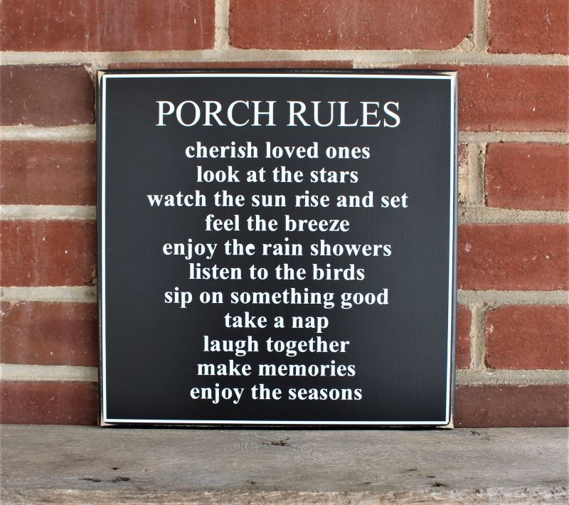Black worn finish square wood sign with white lettering saying.Porch Rules Cherish loved ones Look at the stars Watch the sun rise & set Feel the breeze Enjoy the rain showers Listen to the birds Sip on something good Take a nap Laugh together Make memories Enjoy the seasons